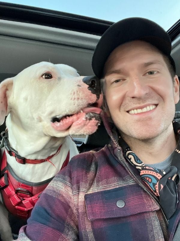 Blake Reichenbach smiling in a selfie next to his white dog